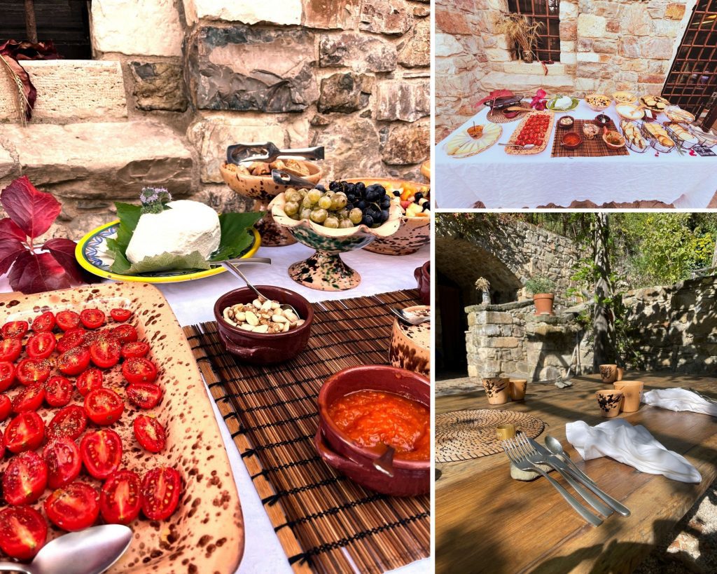 A picturesque outdoor dining setup featuring a variety of Mediterranean dishes, including fresh cherry tomatoes, olives, cheese, nuts, and sauces, arranged on rustic tableware against a stone backdrop. The setting exudes a warm, inviting atmosphere perfect for a leisurely meal.