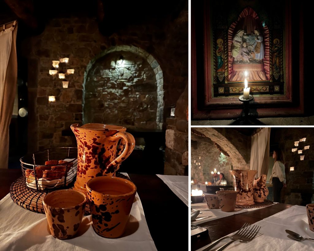 Alt tag: "Cozy candlelit dining setting featuring traditional clay pitchers and cups on a table, with a basket of snacks, rustic stone walls, and an ornate framed painting in the background."