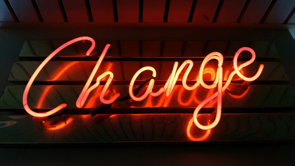Neon sign displaying the word "Change" in vibrant red and orange colors against a reflective background.