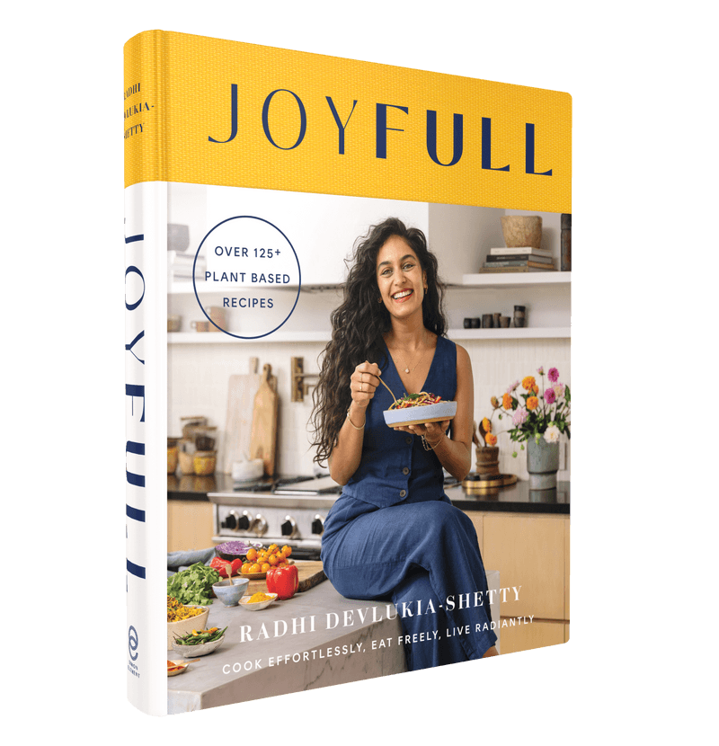A vibrant cookbook titled "Joyfull" by Radhi Devlukia-Shetty, featuring the author smiling while holding a plate of plant-based food in a modern kitchen. The book promises over 125 recipes for effortless cooking.