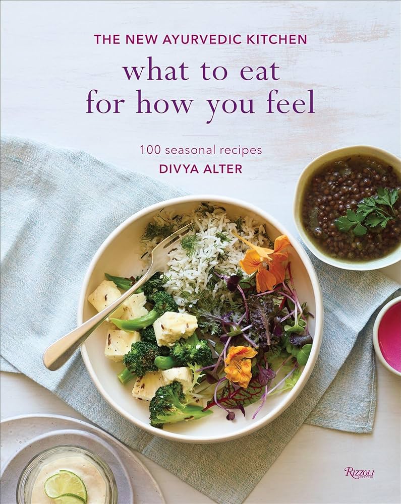 The image is the cover of a cookbook titled "What to Eat for How You Feel" by Divya Alter, featuring a bowl of food with various ingredients. * The title of the book is prominently displayed in large text at the top of the image. + The title reads "what to eat for how you feel". + It is written in a clear and easy-to-read font. * Below the title, there is a subtitle that provides more information about the book's content. + The subtitle reads "100 seasonal recipes". + It suggests that the book contains a collection of recipes organized by season. * In the center of the image, there is a photograph of a bowl of food with various ingredients. + The bowl contains a mix of vegetables, including broccoli and cauliflower. + There are also some type of cheese or tofu cubes in the bowl. + A fork is placed on top of the bowl, suggesting that it is ready to be eaten. Overall, the image effectively conveys the theme and content of the cookbook, which appears to focus on healthy eating and seasonal cooking. The use of a photograph of a delicious-looking dish adds visual appeal and makes the book more appealing to potential readers.