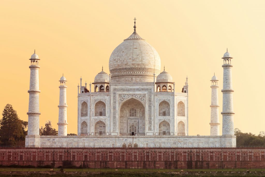 Alt tag: "The Taj Mahal, a white marble mausoleum with a large dome and surrounding minarets, set against a golden sunset sky."