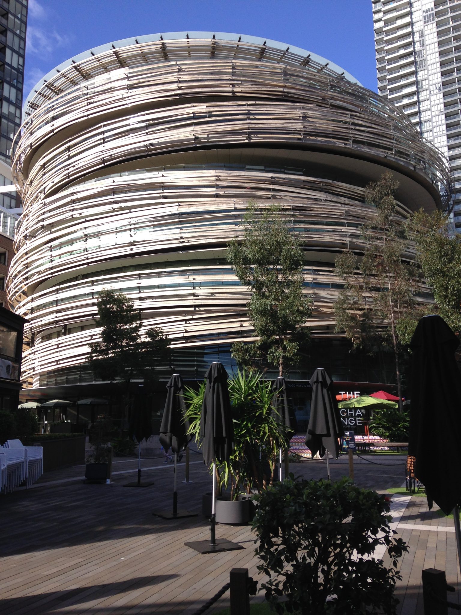 Alt tag: "Modern architectural building with a spiraling wood-and-glass design, surrounded by greenery and outdoor seating areas."
