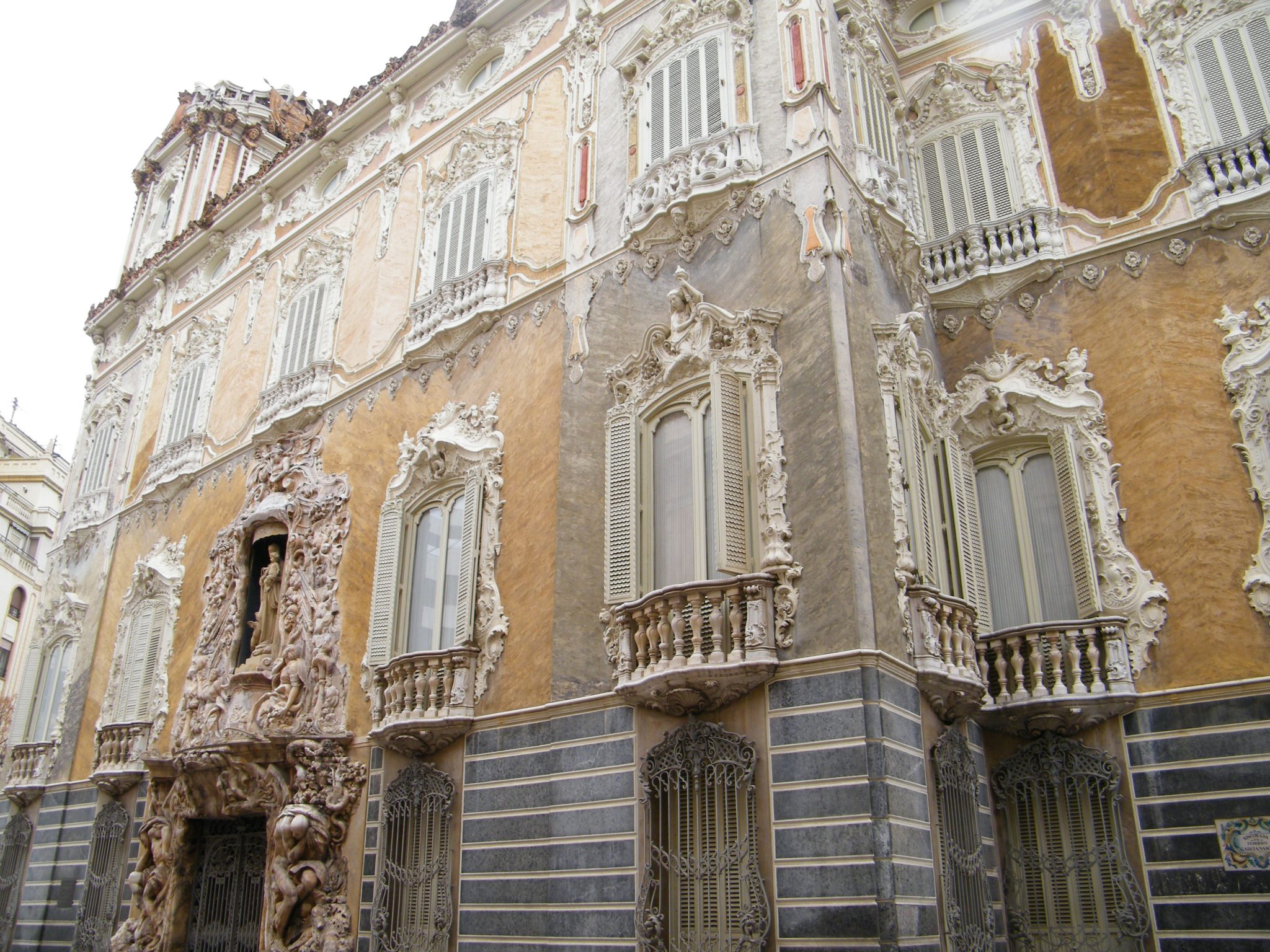 Alt tag: "Facade of an ornate historical building featuring intricate sculptures, decorative balconies, and a mix of textured surfaces in muted colors."