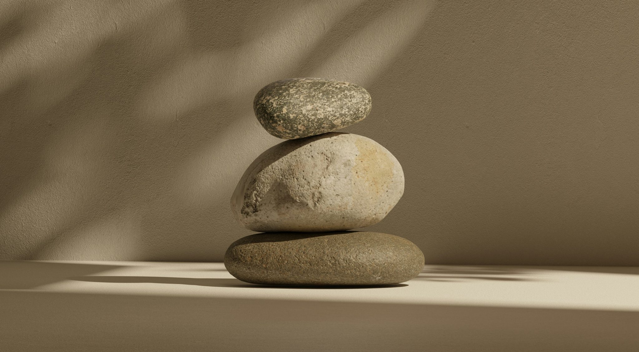 Stacked smooth stones of varying sizes on a neutral surface, with soft shadows and a minimalist background.