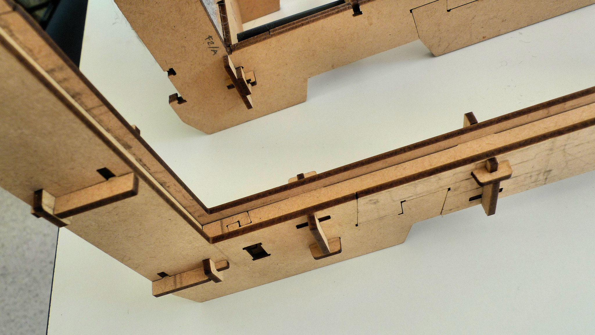 The image presents a close-up view of two wooden pieces, likely from a larger structure or puzzle, with the top piece positioned at an angle and the bottom piece oriented horizontally. * **Wooden Pieces** * The pieces are made of light-colored wood and feature a smooth finish. * They have a rectangular shape with cutouts on their edges for connecting to other parts of the structure. * Each piece has a flat surface, suggesting they may be used as bases or supports within the larger assembly. * **Angle and Orientation** * The top piece is angled upwards, creating a diagonal line that intersects with the bottom piece's horizontal orientation. * This angle adds visual interest to the image and implies that these pieces are part of a 3D structure rather than just flat surfaces. In summary, the image showcases two wooden pieces with distinct orientations, suggesting they are integral components of a larger assembly or puzzle. The smooth finish and rectangular shape of the pieces indicate their intended use as building blocks for a more complex structure.