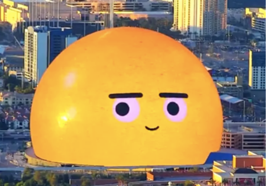 The image presents a close-up view of a yellow emoji with a wide-eyed, neutral expression, situated in front of a cityscape backdrop. * The emoji's facial features are characterized by: * Wide eyes * A small smile * Black eyebrows * In the background, the cityscape is visible through the emoji's face.
