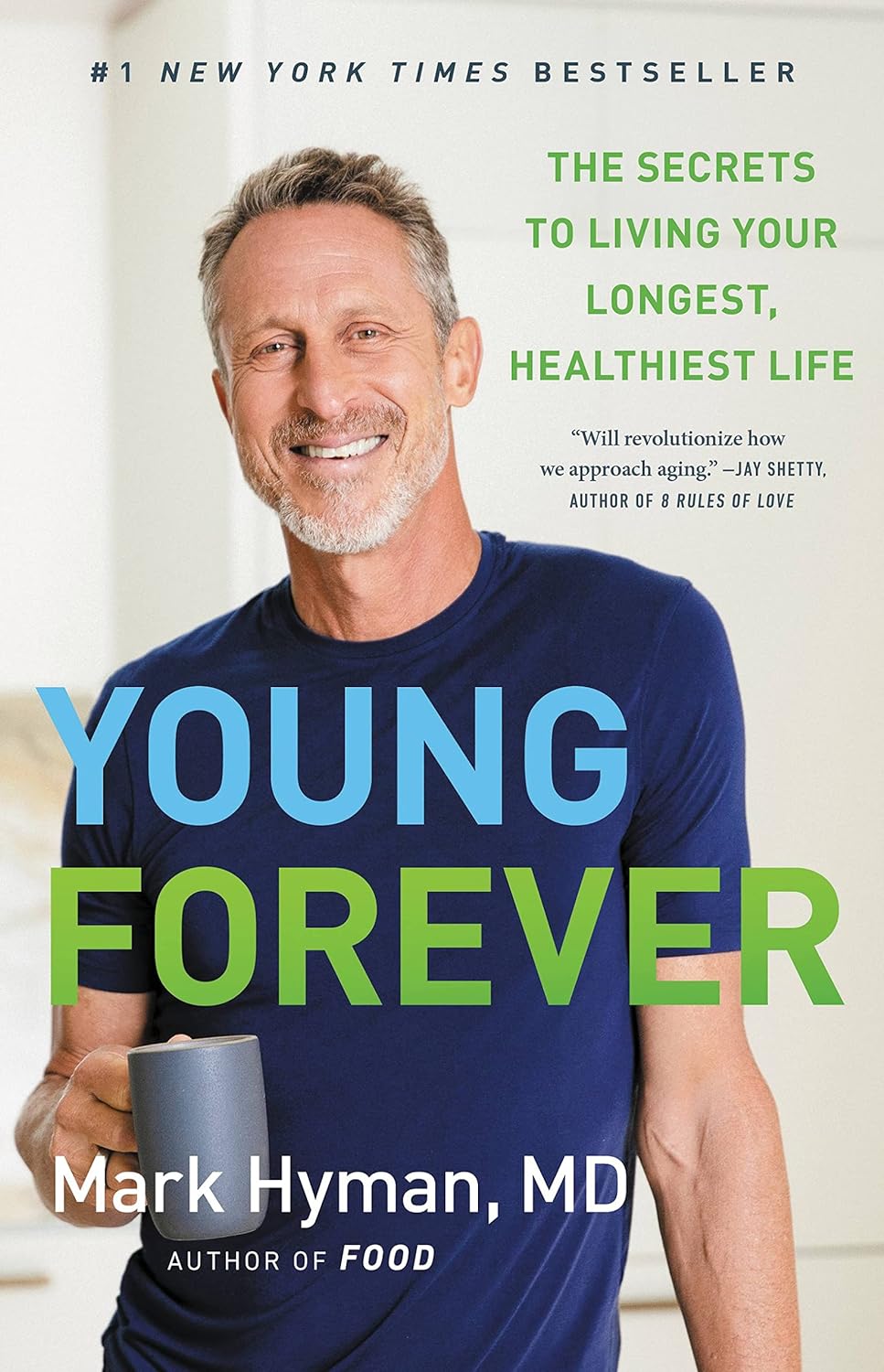 The image is the cover of the book "Young Forever" by Mark Hyman, MD. * A man holding a mug: + The man has short gray hair. + He is wearing a blue t-shirt. + He is smiling and looking at the camera. + He is holding a white mug in his right hand. * The title of the book "Young Forever": + The title is written in large, bold letters across the center of the image. + The words are colored in light blue, green, and yellow. + The font size decreases as it moves from left to right. * A man's torso: + The man's torso is visible on the right side of the image. + He is wearing a blue t-shirt. + His arm is bent at the elbow, with his hand resting on his hip. The image suggests that the book "Young Forever" is about maintaining youth and vitality as one ages. The use of bright colors and a smiling man holding a mug may convey a sense of positivity and optimism.