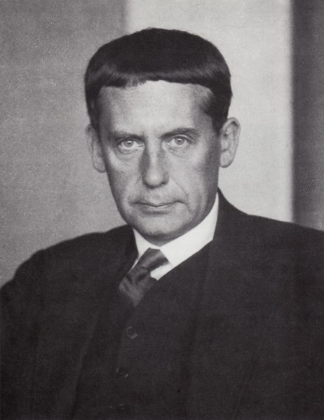 Black and white portrait of a man with short hair and a serious expression, dressed in a suit and tie.