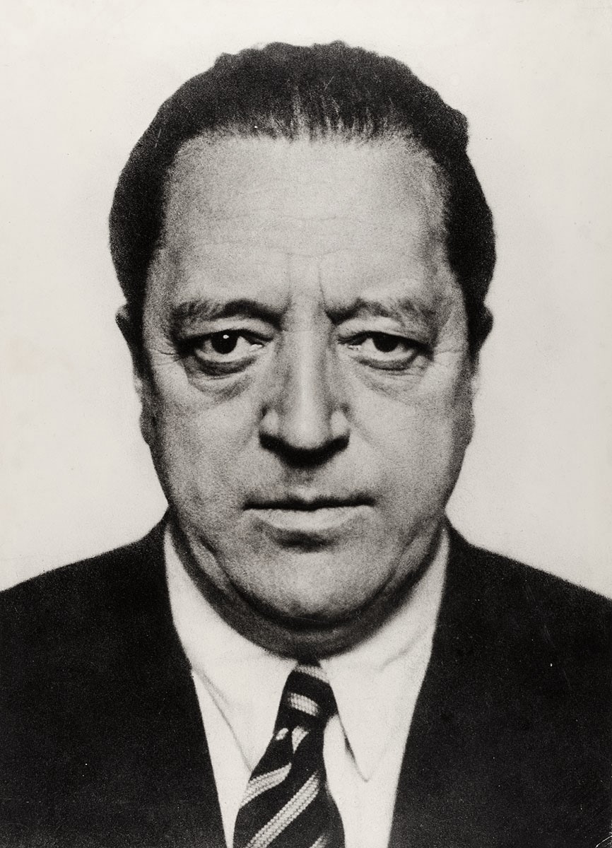Portrait of a middle-aged man with a stern expression, wearing a dark suit and striped tie, against a plain background.